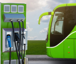 Elektroauto uzlādes stacija, fonā zaļš autobuss